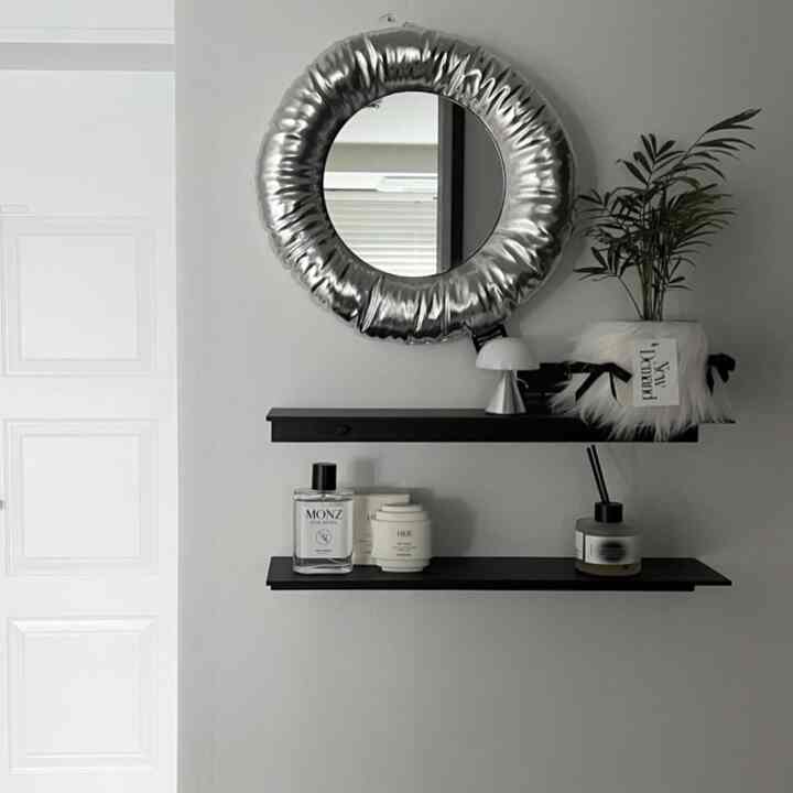 白い壁に黒い棚が2つ、銀色のクッション縁の丸い鏡が配置されたミニマルな玄関インテリア