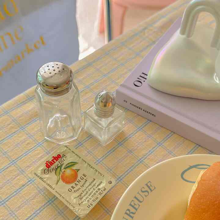 黄色のチェック柄テーブルクロスの上にヴィンテージのガラス調味料瓶とおうちカフェ風の小物が配置されたキッチンスペース