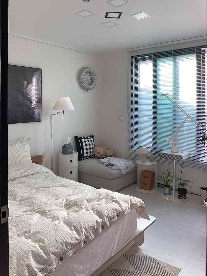 Bright white and ivory toned bedroom featuring a bed and black blinds in a simple modern style space