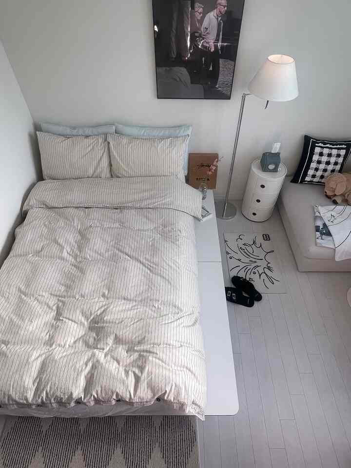 Neutral-toned small bedroom featuring beige bedding, white floor lamp, and sofa creating a cozy atmosphere