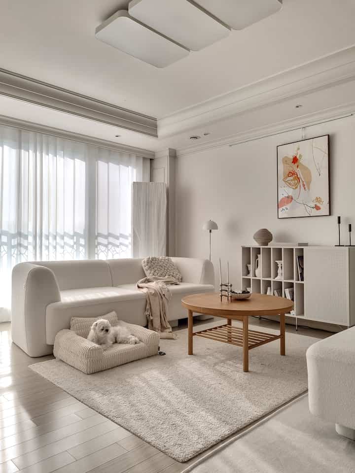 白とナチュラルカラーの印象的なリビング、ブークレのモジュールソファと丸いコーヒーテーブル、ペット用ベッドが配置された落ち着いた空間