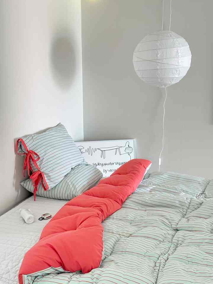 A simple bedroom interior with bright white walls featuring striped bedding in orange tones