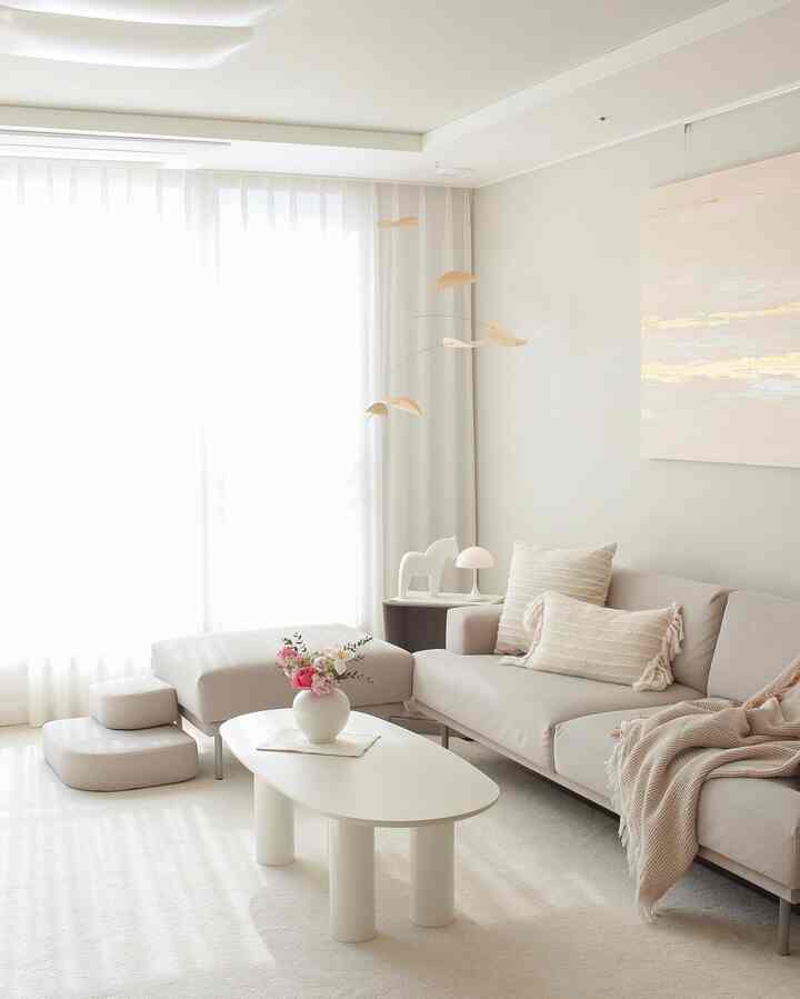 明るく柔らかなアイボリーとベージュの色調のリビング、ファブリックソファと白いコーヒーテーブルに花瓶が置かれたミニマルでナチュラルな雰囲気のインテリア