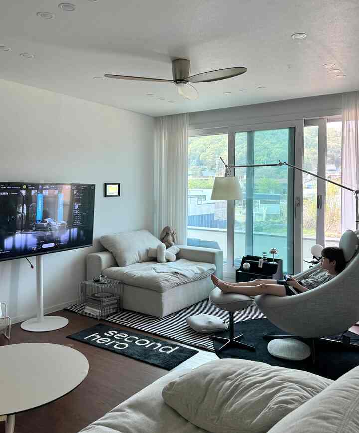 白と木目調のリビング、カンポソファとゲーミングチェアが配置された落ち着いた雰囲気の空間、窓の外に自然の景色