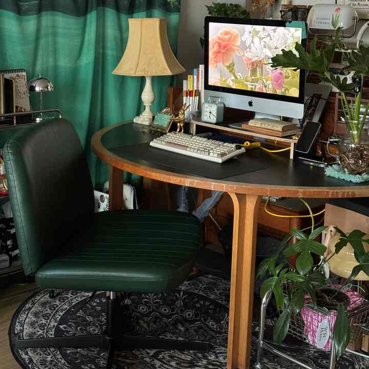 ティール色のカーテンと木製デスク、レザーオフィスチェアが配置されたホームオフィスの雰囲気あるインテリア