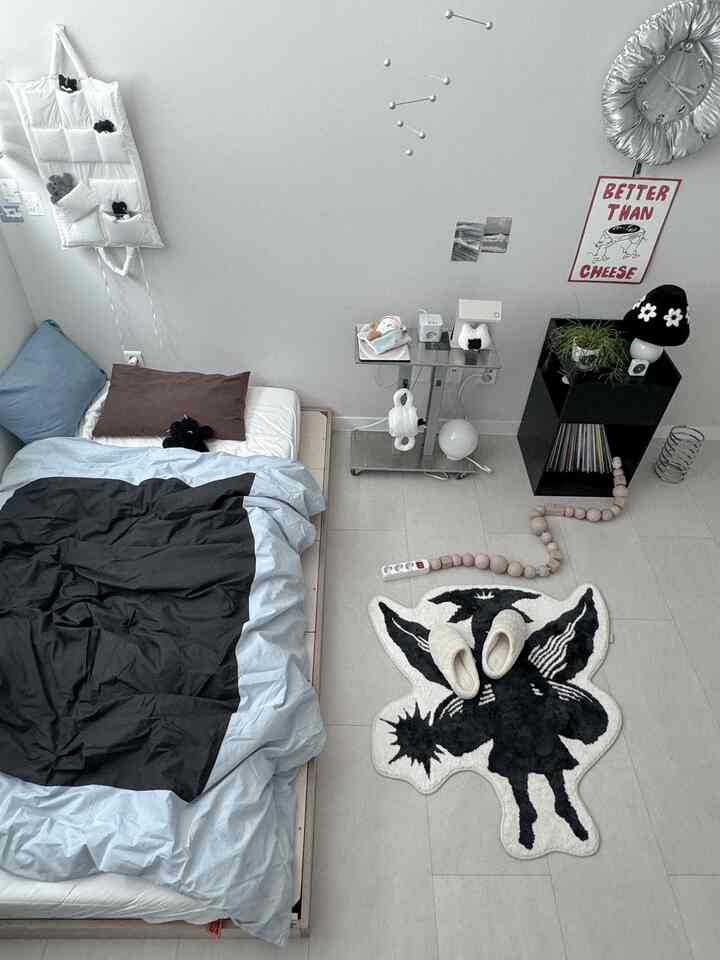 白とグレーのトーンの狭い寝室。低いベッドと猫をモチーフにした小物、特徴的なラグや壁時計が配置されたモダンなインテリア。