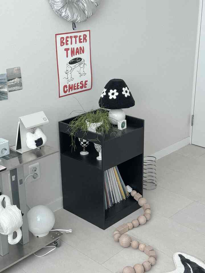 白と黒のトーンのリビングコーナー、サイドテーブルや植物、ポスターが配置されたモダンで清潔感のある空間