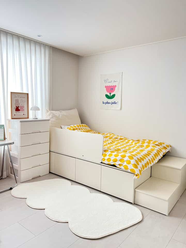 White and yellow toned kids' room featuring lemon-patterned duvet, storage bed, fabric poster, and soft rug in simple modern style
