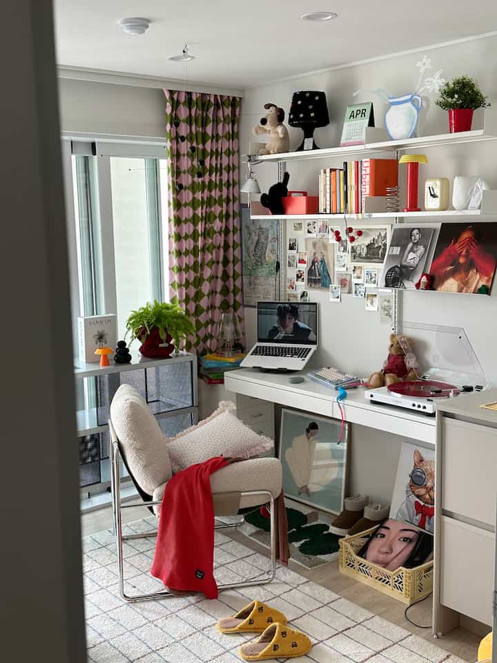 Bright white and wood-toned home office study featuring a mid-century modern chair, spacious desk, and walls adorned with posters and art creating a cozy atmosphere
