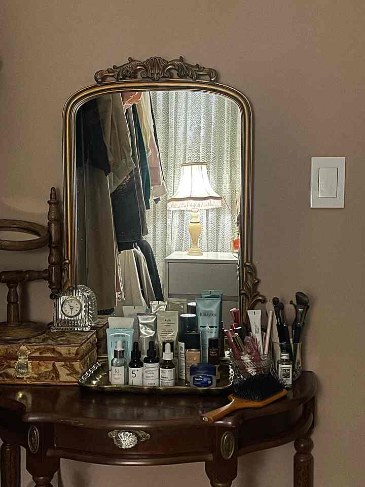 暖かいベージュ色調の壁と木目調のヴィンテージ化粧台が配置されたウォークインクローゼット、鏡と多様な化粧品が調和する雰囲気のあるインテリア