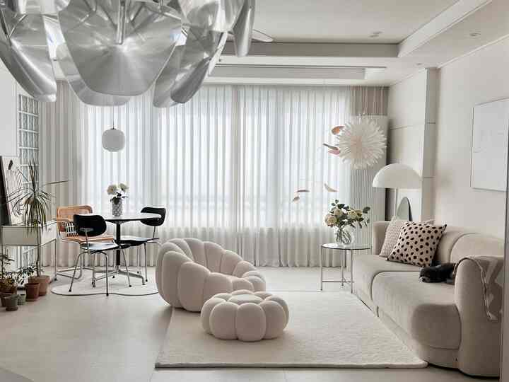 Bright and soft white and ivory toned living room featuring curved sofa, curtains, and pendant lights creating a cozy atmosphere