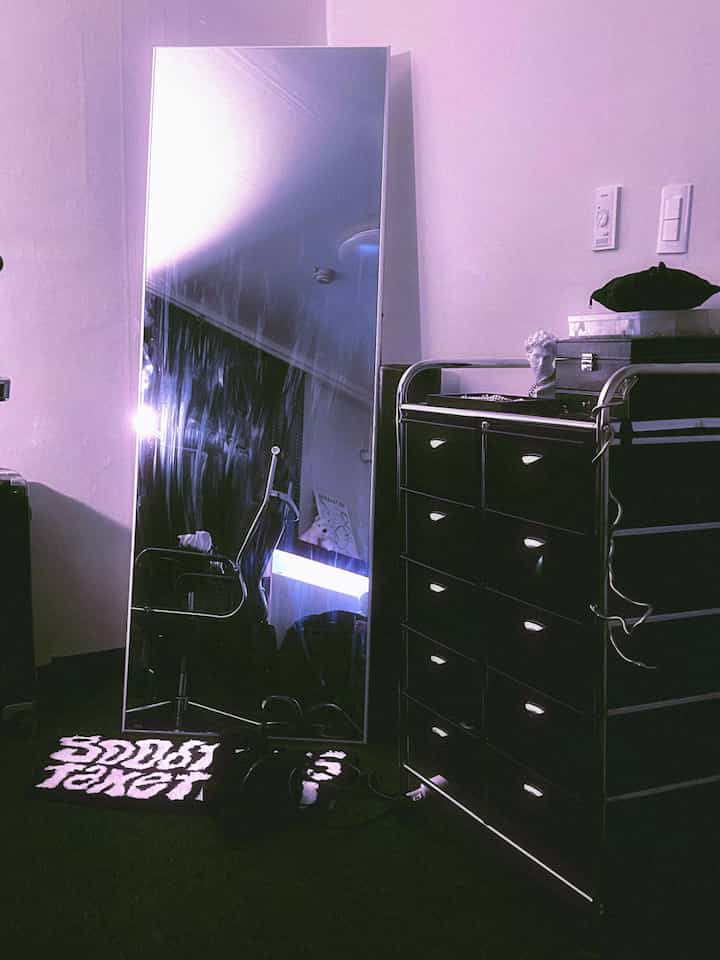 黒とシルバーのトーンのワンルーム、5段引き出しタローリーと全身鏡が配置された現代的でミッドセンチュリーモダンなインテリア