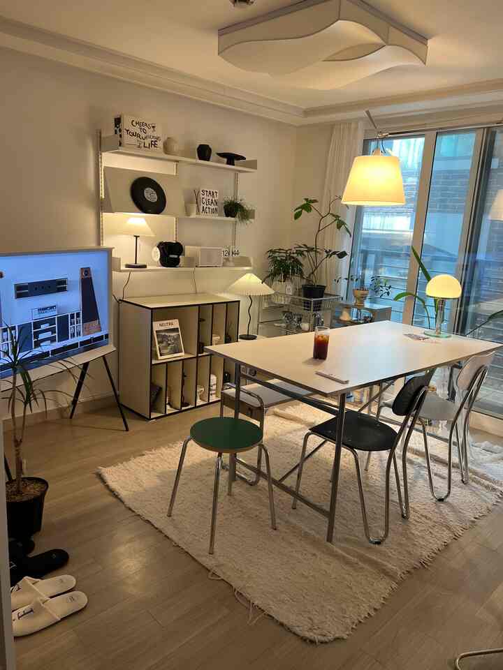 Modern living and dining room in white and wood tones, featuring a dining table with chairs and various plants, creating a cozy atmosphere