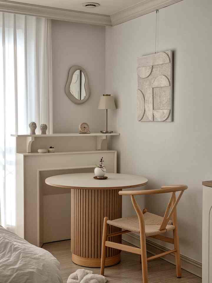 ベージュとアイボリーのトーンの小さなワンルーム寝室、木製の円形テーブルと椅子が配置されたナチュラルモダンなおうちカフェ空間