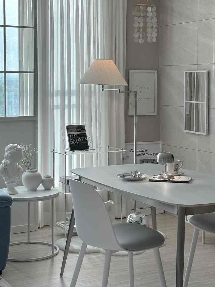 White-toned living dining area featuring a simple dining table, lighting fixtures, picture frames in a mid-century modern style interior