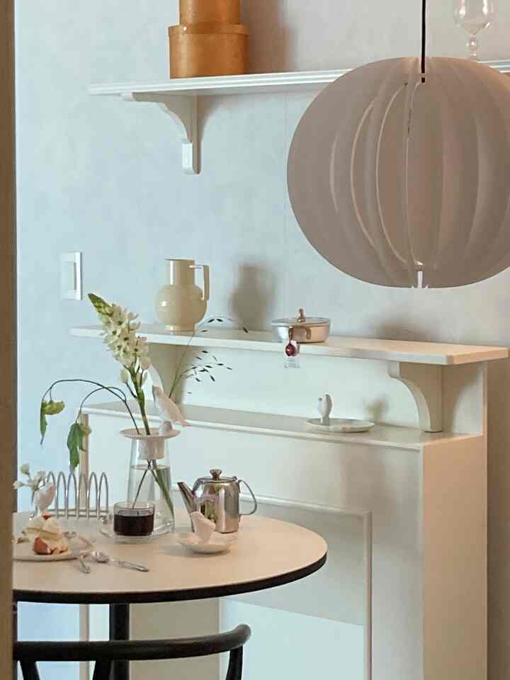 白を基調としたダイニングルーム、中央にラウンドテーブルとコーヒー用品が配置された、自然でミニマルな印象のホームカフェ空間