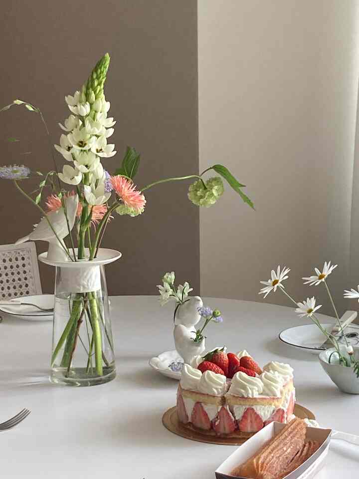白とベージュの色調のダイニング、中央に花瓶とケーキを置いたダイニングテーブルが配置された清潔で落ち着いた雰囲気の空間