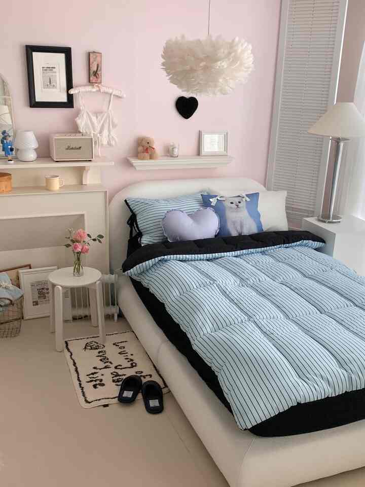 Bedroom with pink walls and blue striped bedding, featuring heart-shaped and cat-print cushions in a cozy setting
