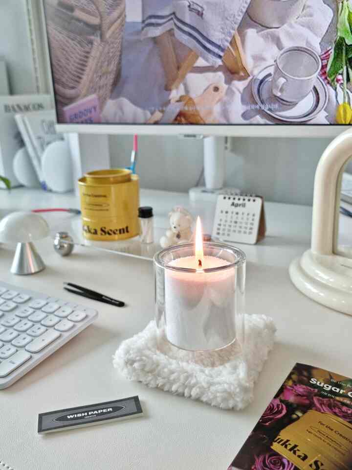 White-toned home office desk featuring a lit white candle and mid-century modern mood lamp in a neat workspace