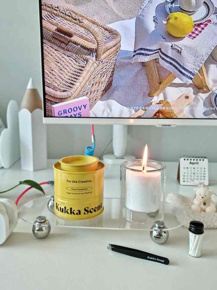 White-toned home office desk featuring a transparent tray with a yellow candle container and a lit white candle, creating a clean desk interior