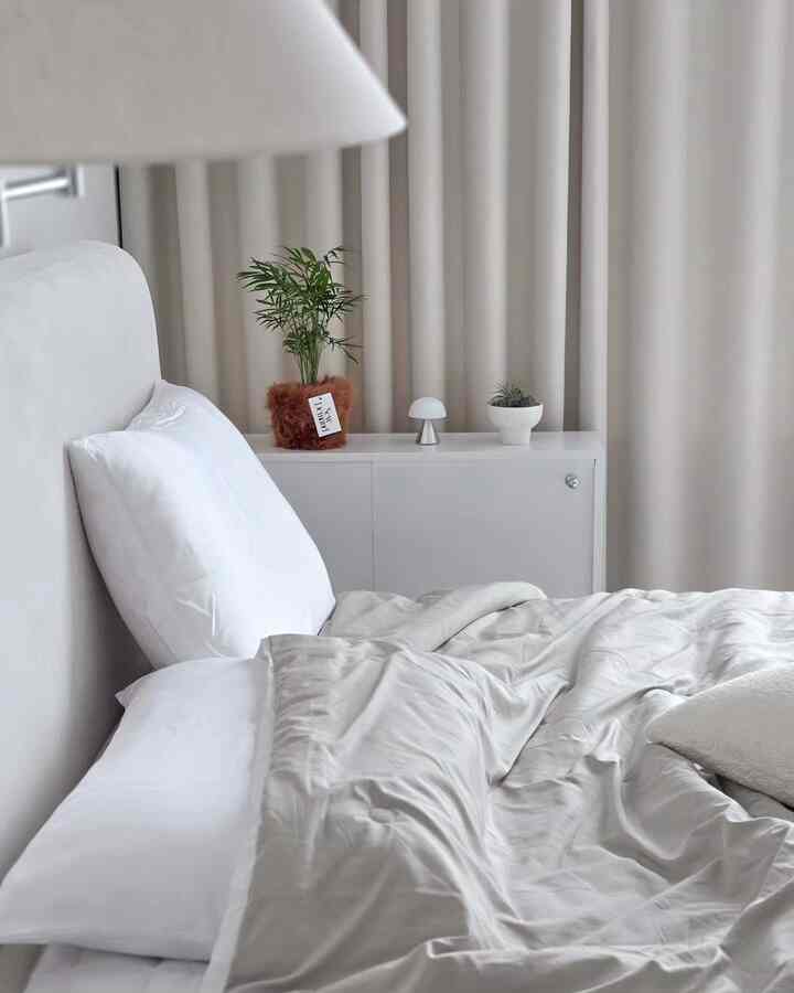 A white and beige toned bedroom featuring a white bed and blackout curtains, creating a clean and cozy atmosphere