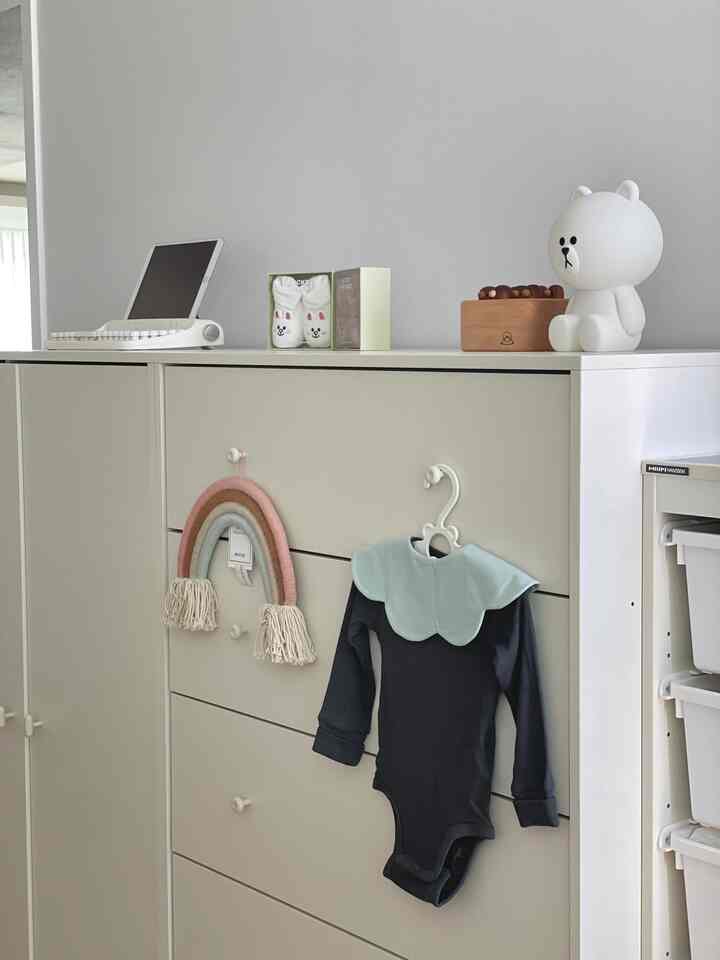 明るいホワイトとベージュのトーンが特徴的な赤ちゃん部屋、ハンセムの収納家具と整ったベビー服や小物が配置された清潔感のあるインテリア