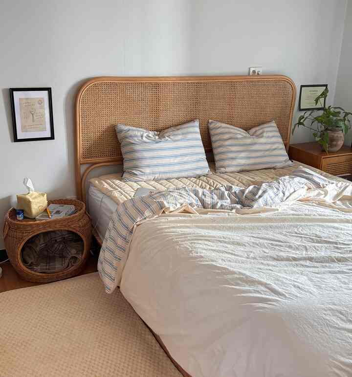 ナチュラルなベージュ色調の寝室、ラタンのヘッドボードとナイトテーブル、心地よい寝具とカーペットが配置された雰囲気のあるインテリア