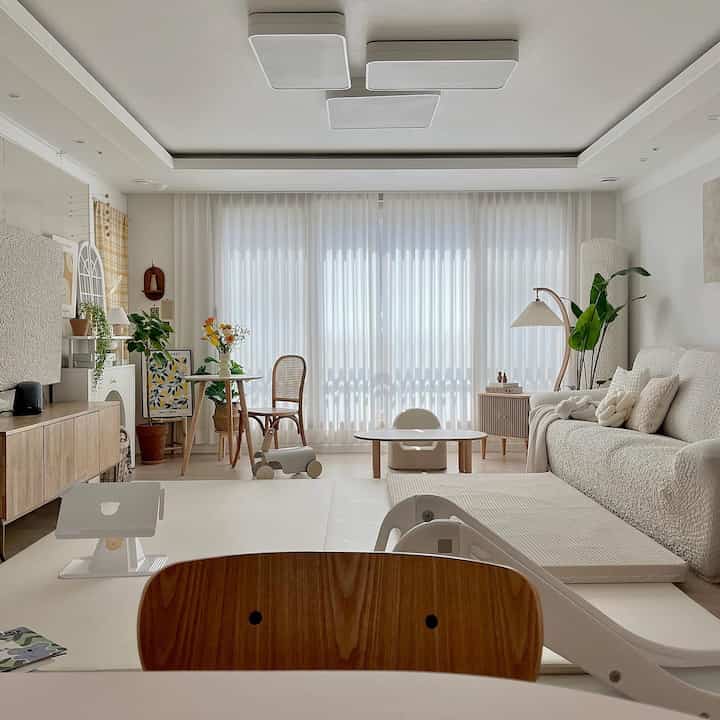 明るくナチュラルな色調のリビング、木製家具と白いソファ、カーテンが調和した落ち着いた空間