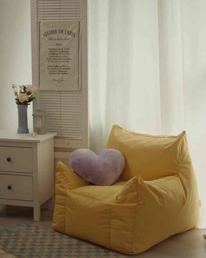 Cozy studio apartment space with white curtains, a nightstand, yellow bean bag, and purple heart cushion