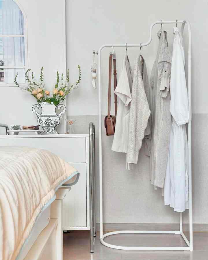 明るく清潔感のあるホワイトトーンの寝室、アーチ型のホワイト鉄製ハンガーラックと整然としたベッドが配置されたミニマルなインテリア