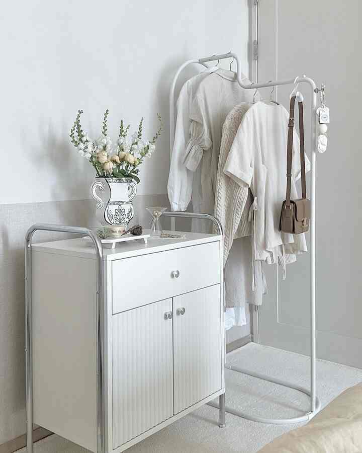 白を基調としたウォークインクローゼット、衣類ラックと収納キャビネットが配置され、自然な花瓶がアクセントのある雰囲気の空間