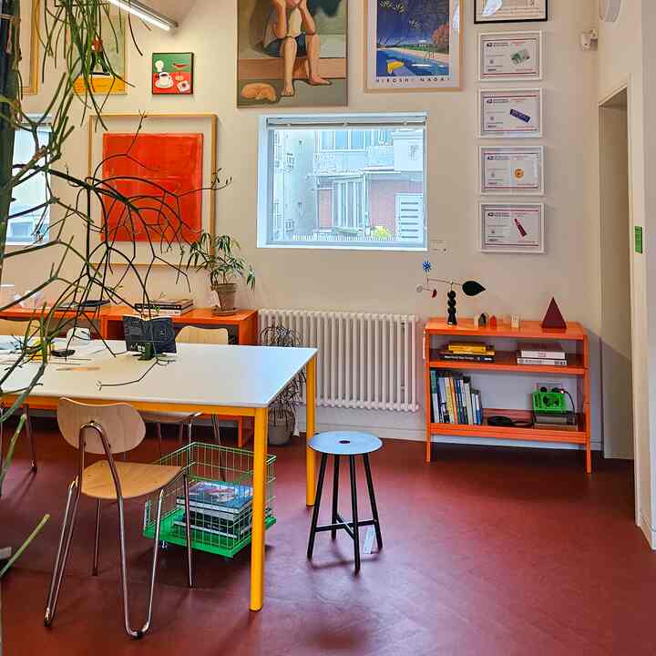 明るいオレンジと赤のトーンのホームオフィス、白いデスクと棚、壁のアートや植物が配置された雰囲気のある作業空間