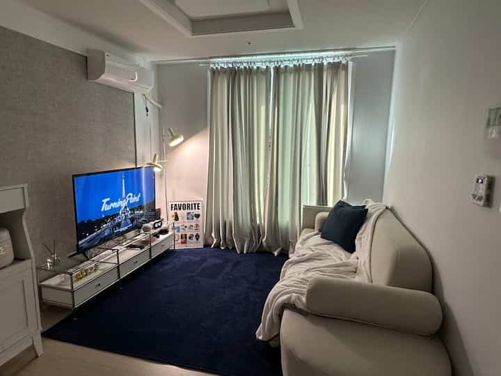 白とネイビー、ベージュトーンの小さな2部屋のリビング、ベージュのソファとネイビーのラグが配置されたミッドセンチュリーモダンなインテリア