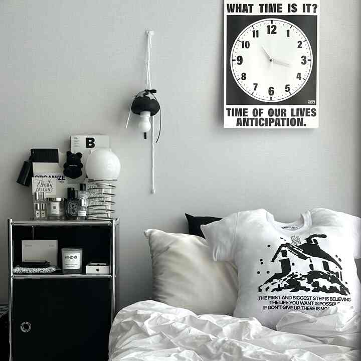 Monotone white and black bedroom featuring simple nightstand and framed clock, minimalist atmosphere