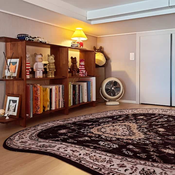 温かみのあるウッドトーンとブラックラグのロフトスタイルワンルーム寝室、棚とムードライトが配置された雰囲気のある空間