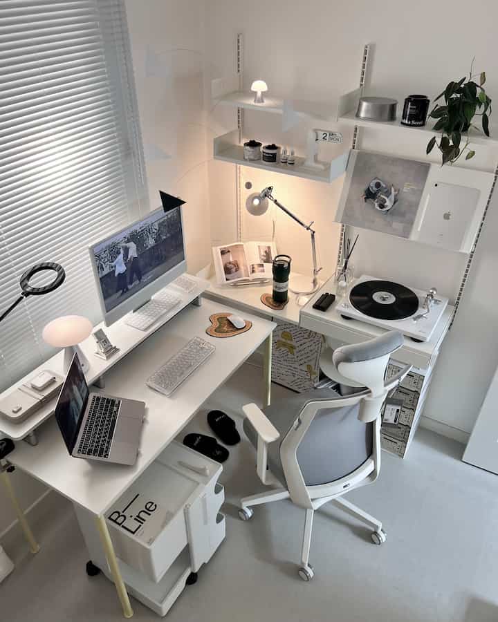 明るく清潔なホワイトトーンのホームオフィス、モニターとノートパソコン、デスクチェア、壁棚とターンテーブルが配置されたミニマルなデザイン