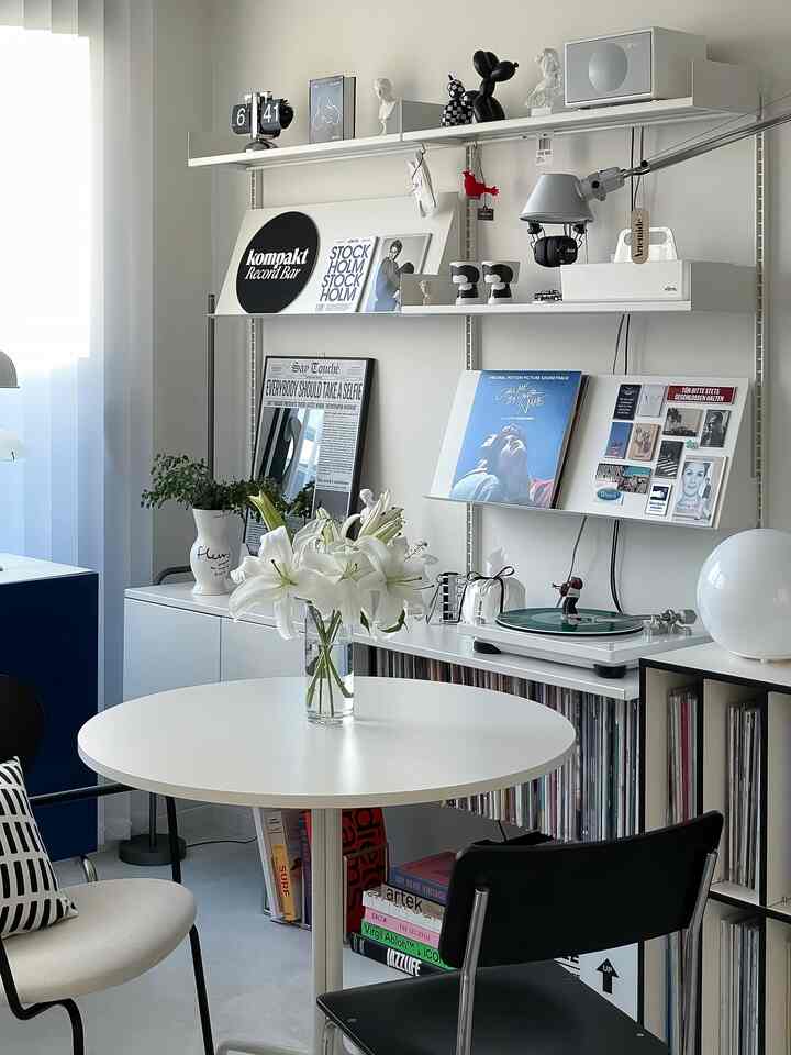 ホワイトトーンのリビング、丸テーブルとポスター、棚の上のターンテーブルとオブジェが配置されたモダンな雰囲気のインテリア