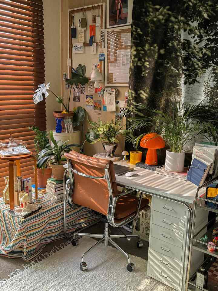 温かみのある木目調と白い家具が調和するワンルームのホームオフィス、多様な植物とポスターで飾られた空間