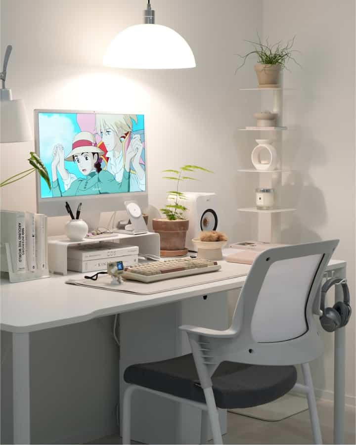 White-toned compact home office featuring iMac, desk, and shelf with plants, creating a neat and clean workspace interior