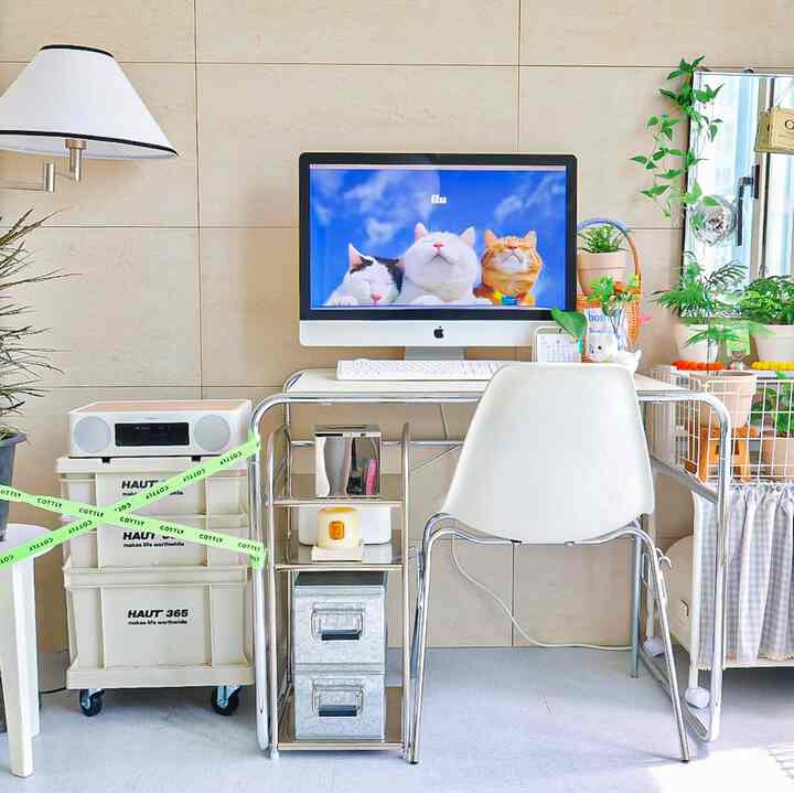 Bright beige wall home office featuring a white desk, silver metal shelving, and multiple indoor plants with a clean atmosphere