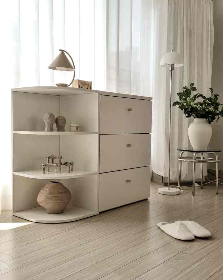 Light white and beige toned living room featuring minimalist storage cabinet, floor lamp, and a plant creating a cozy atmosphere