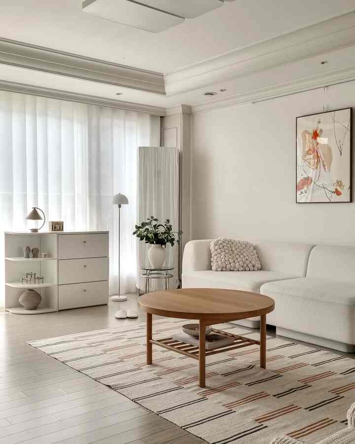 Clean living room in white and wood tones featuring a sofa and round coffee table with a cozy atmosphere