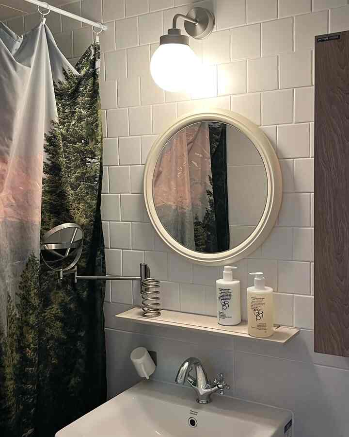 白いタイル壁と丸い鏡、森のデザインのシャワーカーテンが配置されたシンプルなバスルームインテリア