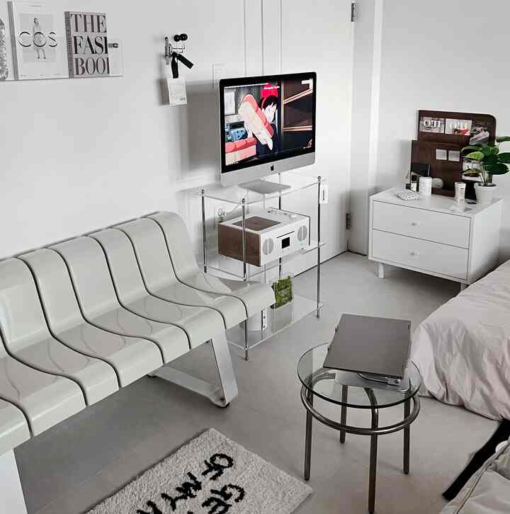 白を基調としたリビング、透明な棚の上にあるiMacと白いベンチが配置されたミニマルなインテリア