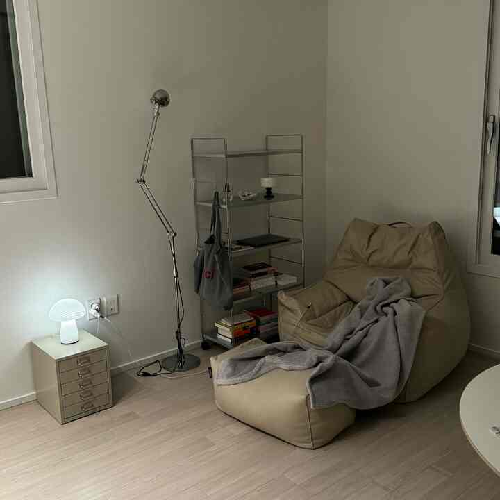 ナチュラルカラーの小さな部屋、ベージュのビーズクッションソファとメタルの棚、フロアランプが配置されたシンプルモダンでリラックスできる空間