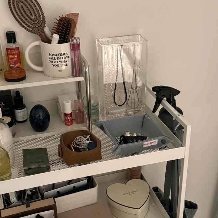 ホワイトの金属棚と透明なアクリルのネックレスホルダー、ブラウンのフェルトトレイが配置された整理された収納スペース