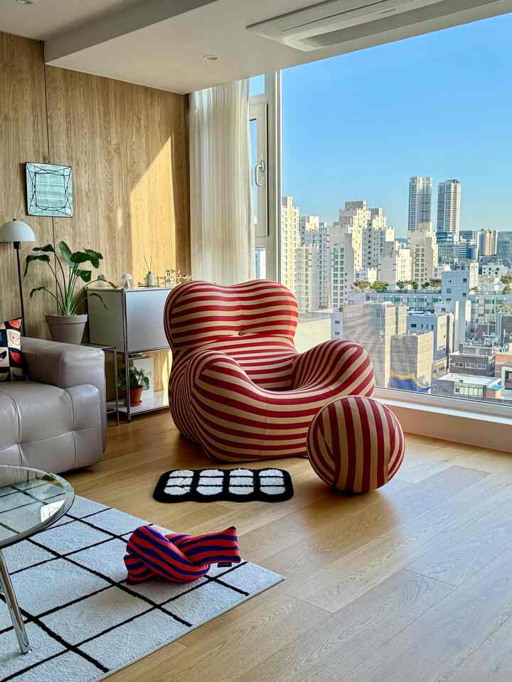 Bright natural wood-toned living room featuring a unique red striped armchair and matching round stool in a cozy setting