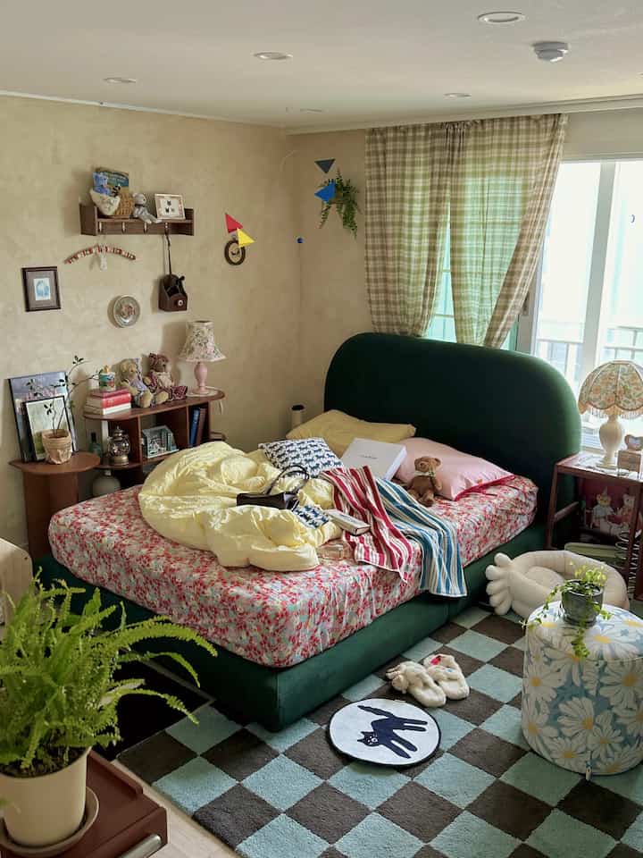 ベージュ色の壁と木製家具が調和した寝室、グリーンのファブリックベッドとチェック柄カーテンが雰囲気のある空間を演出