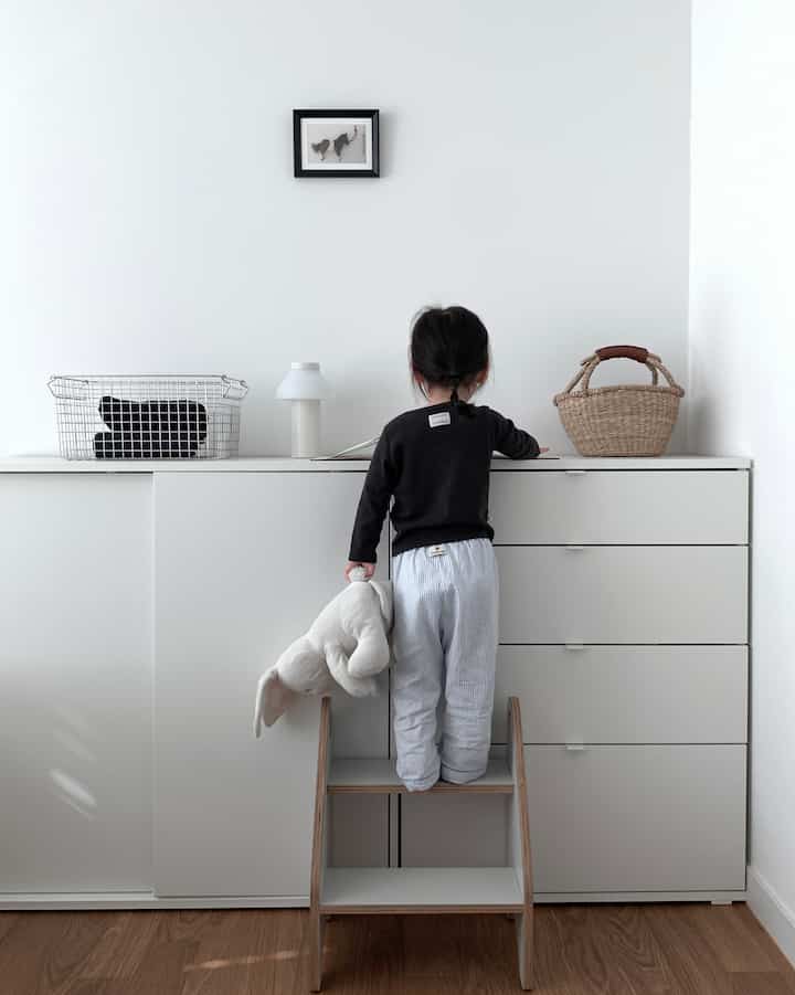 白と木目調が調和する子供部屋、スライドワードローブとチェストが配置されたシンプルで印象的な空間