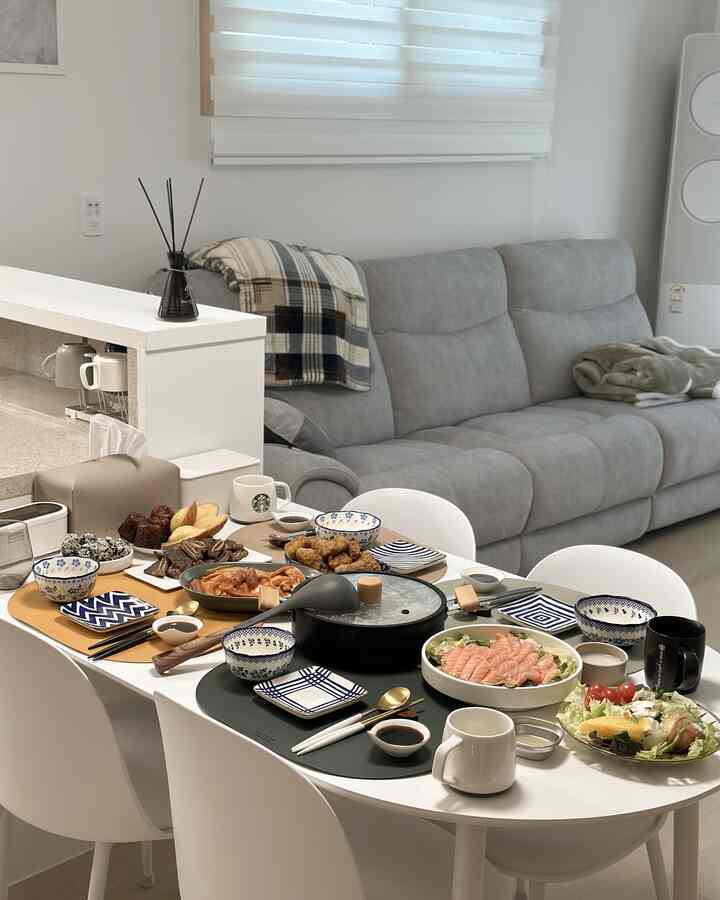 白とグレーのトーンのリビング、モダンなソファと食卓に様々な料理が並べられたホームパーティーのある印象的な空間